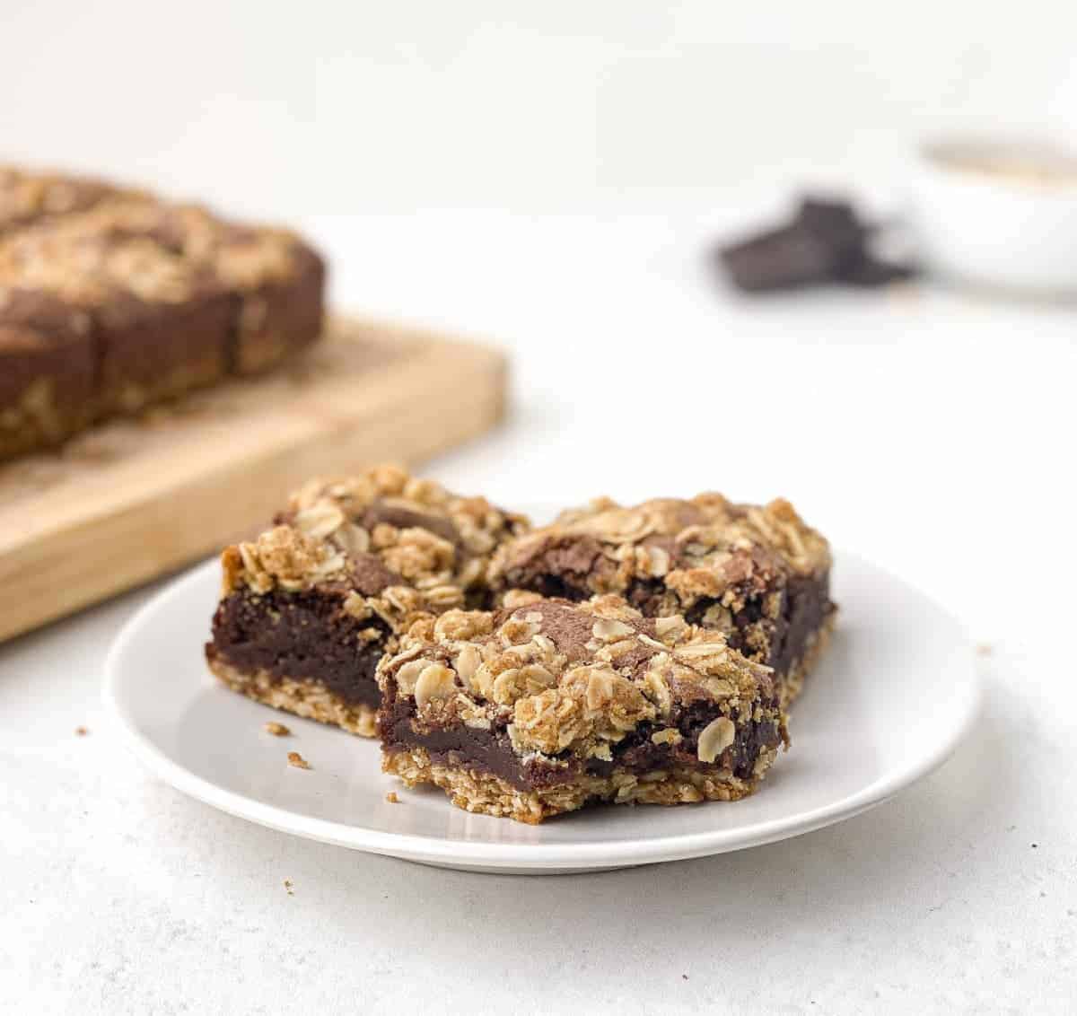 Three Oatmeal Brownies on a white plate with a bite missing from one of them.