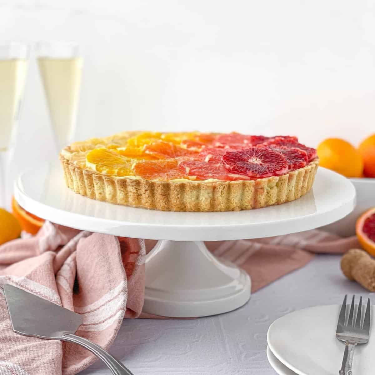 Champagne Citrus Tart on a white stand with champagne and citrus nearby.