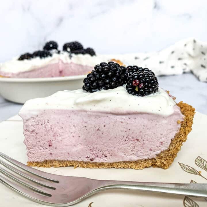 Slice of Blackberry Cream Pie on a white plate with fresh blackberries on top.
