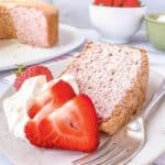 Slice of Strawberry Angel Food Cake on a plate with whipped cream and fresh strawberries.
