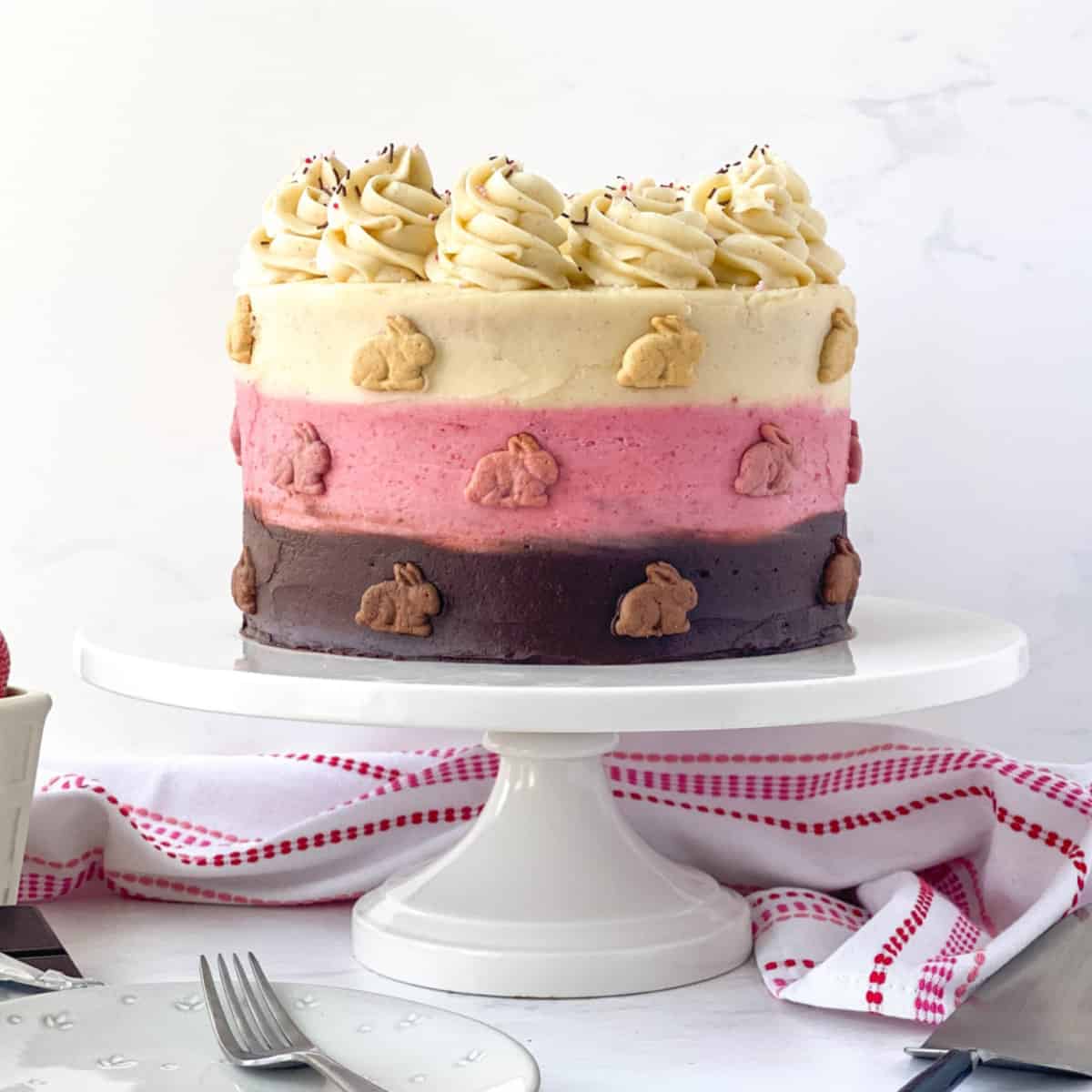 Neapolitan Cake with graham bunnies on the outside on a white cake stand.