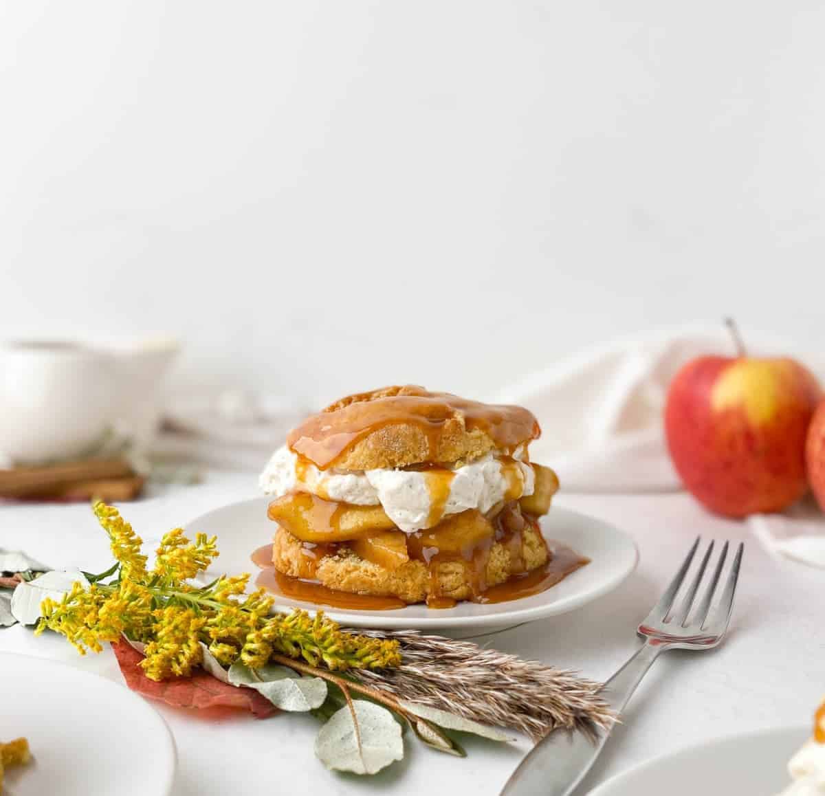 Caramel Apple Shortcake on a white plate near yellow flowers with apples in the background