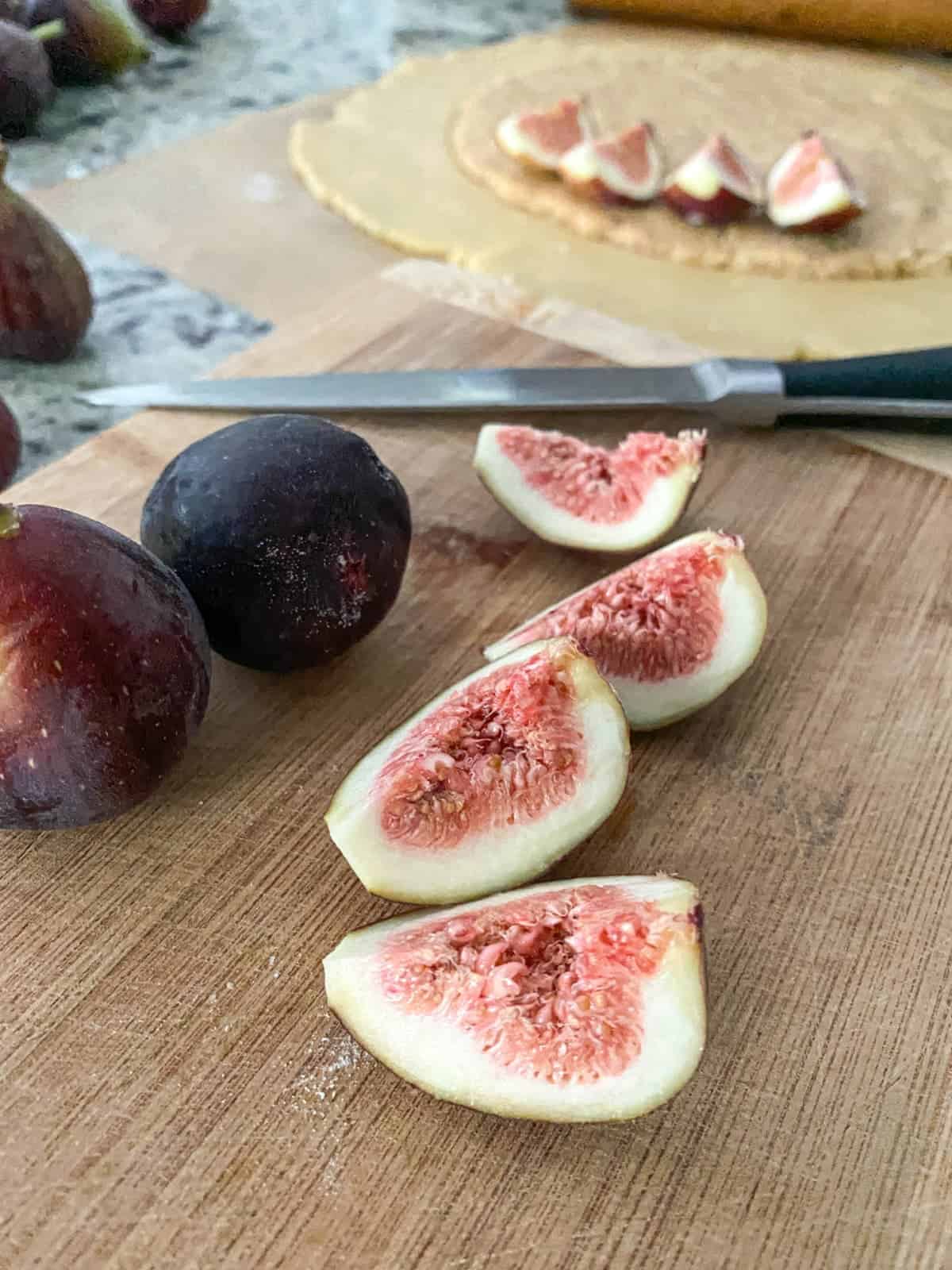 whole and cut figs on a wooden cutting board with a knife in the background