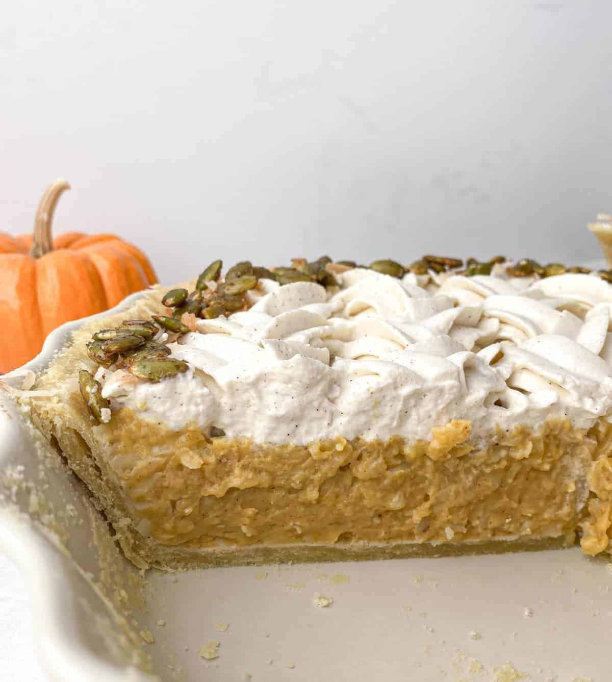 Pumpkin Coconut Cream Pie sliced in the pie plate with a small pumpkin in the background
