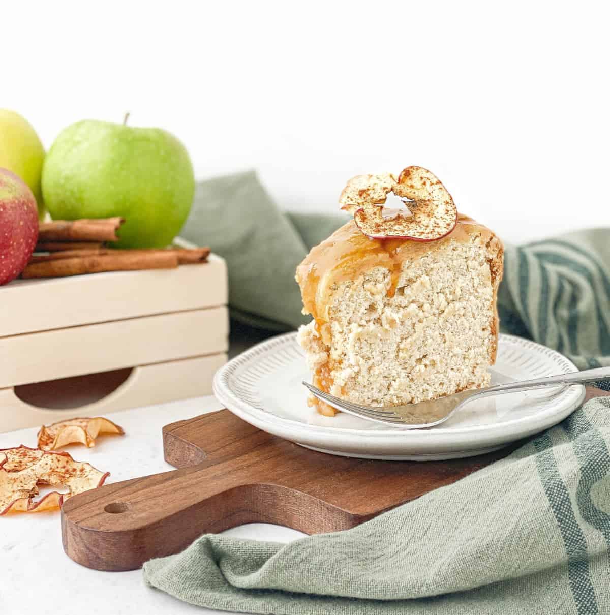 Slice of Caramel Apple Angel Food Cake on a plate with apples and cinnamon sticks nearby