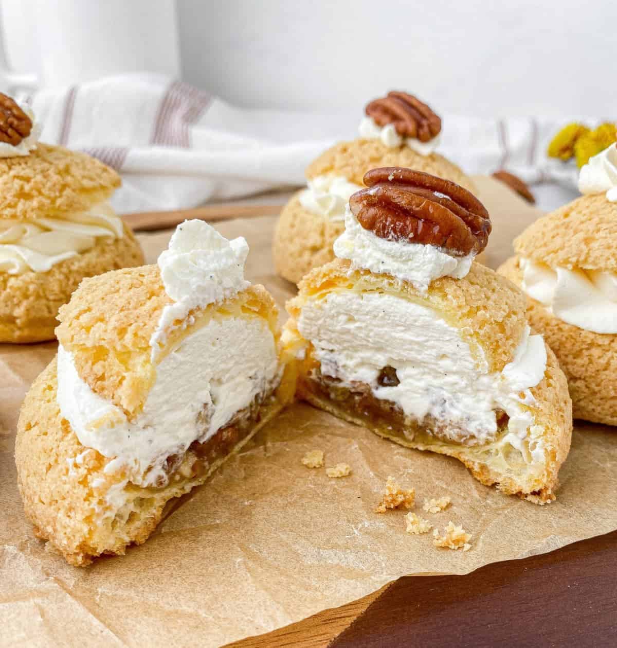 Two halves of a Pecan Pie Cream Puff on a serving board with more cream puffs in the background