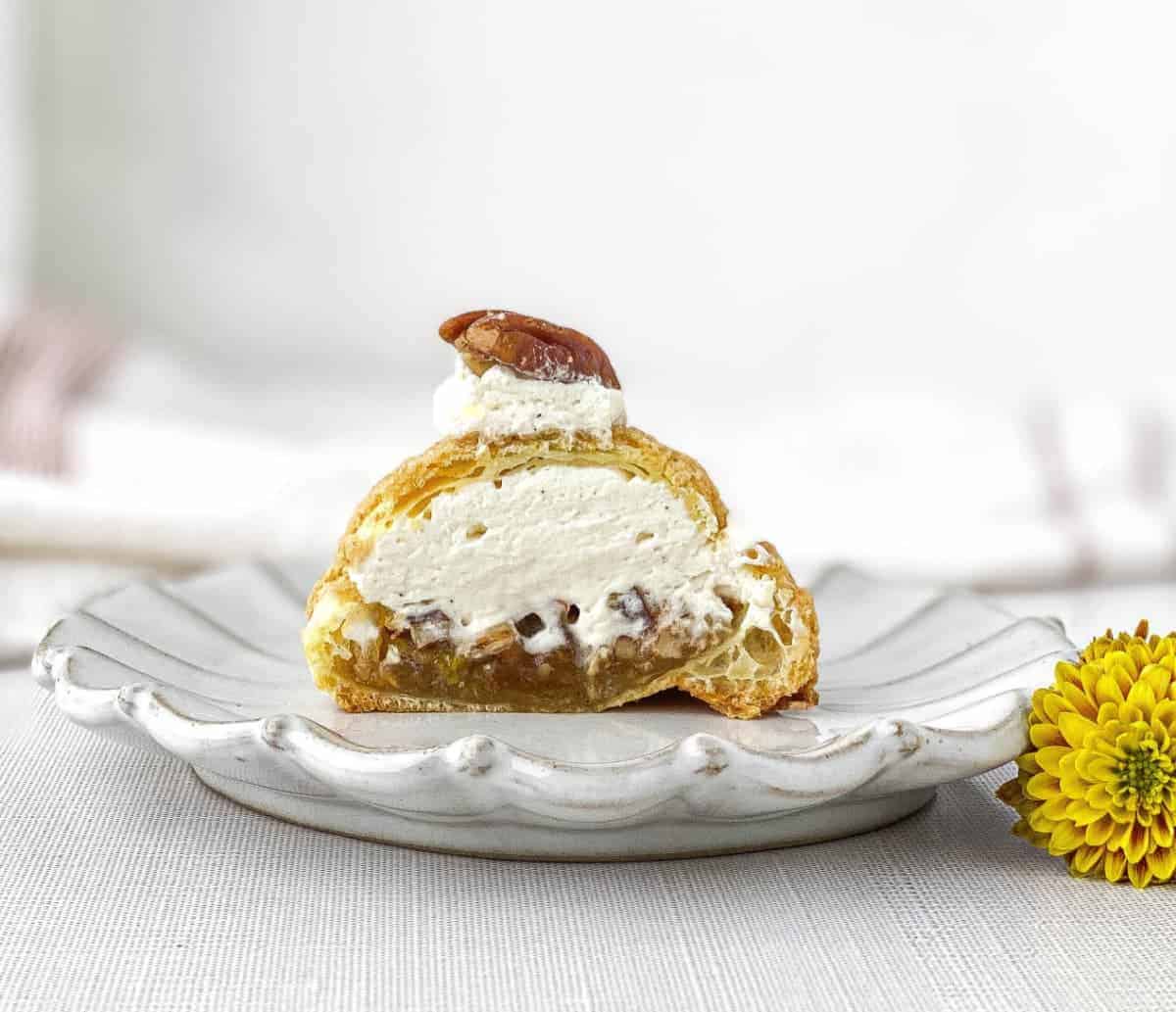 Half a sliced Pecan Pie Cream Puff on a plate with yellow mum flowers nearby
