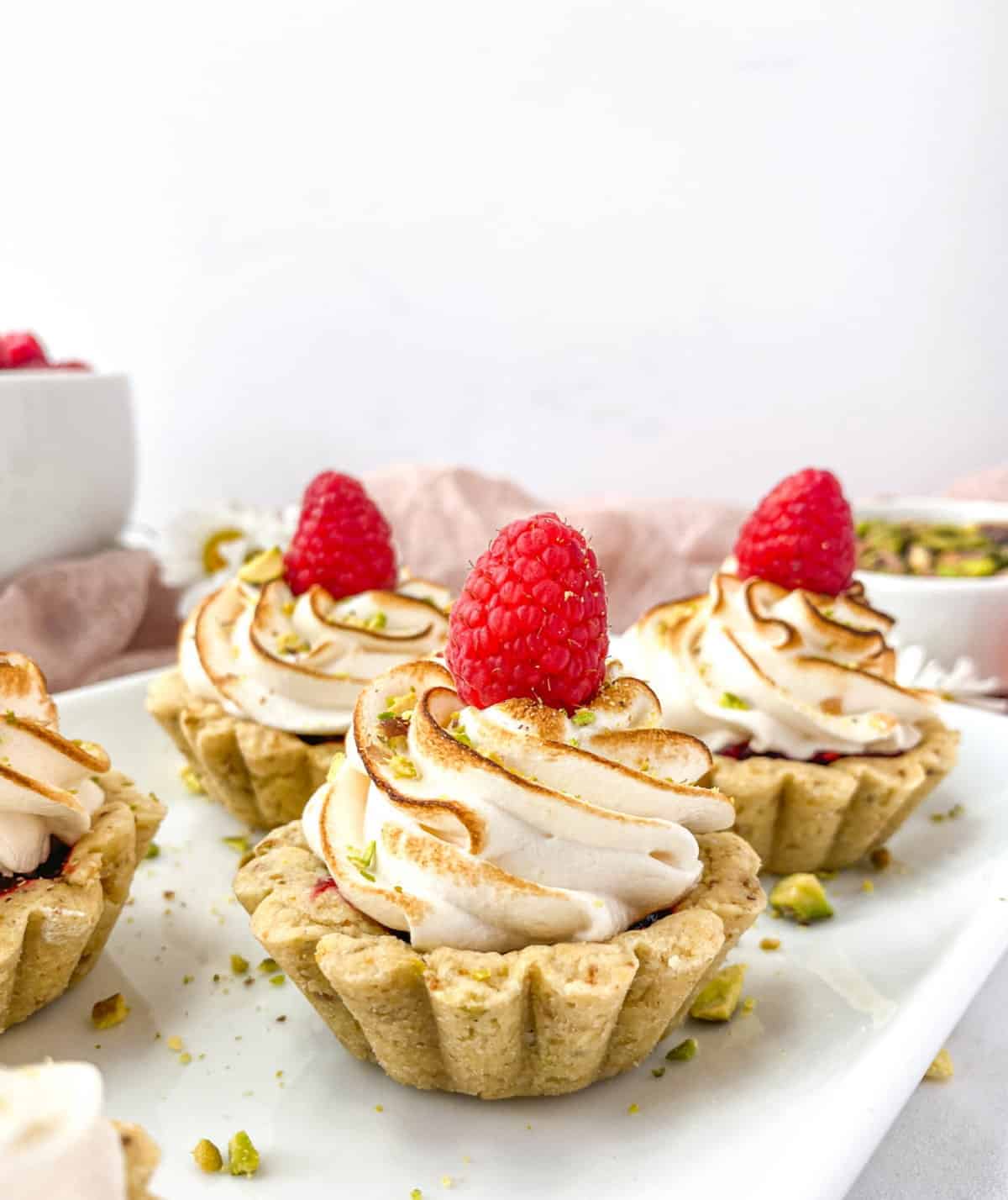 Several Raspberry Pistachio Tartlets linesd up on a white plate