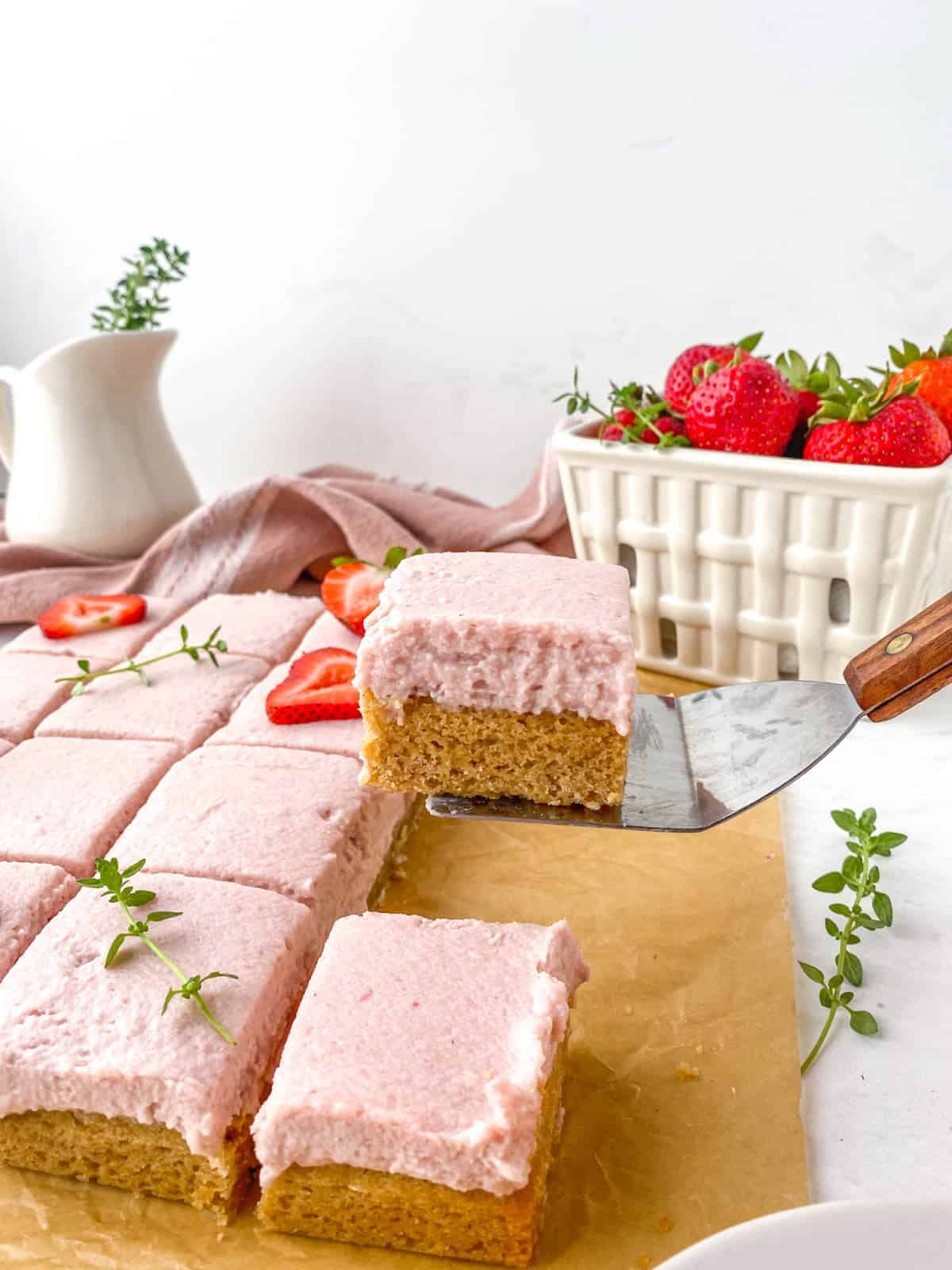 Strawberry Thyme Blondie being lifted with a small spatula with strawberries and thyme in the background