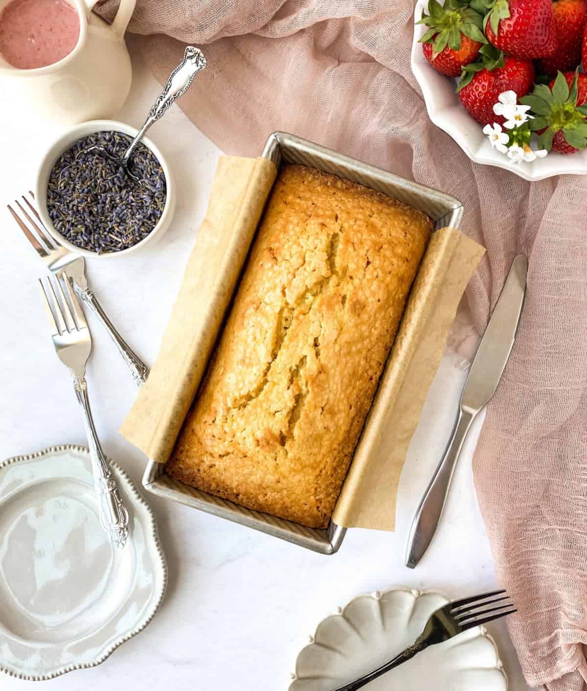 Unglazed Lavender Pound Cake in pan with lavender and strawberries nearby.