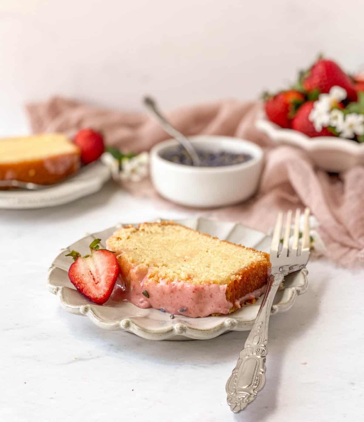 Slice of Lavender Pound Cake with Strawberry Glaze on a fluted plate with a silver fork.