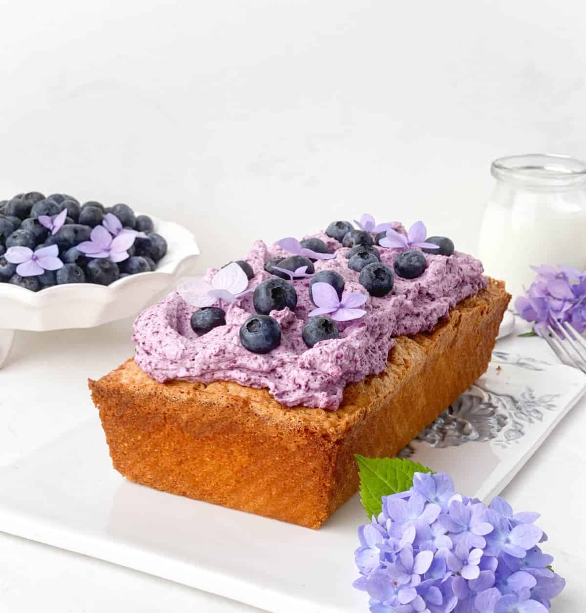 Blueberry Cornmeal Pound Cake on a white tray with blueberries and a glass of buttermilk.