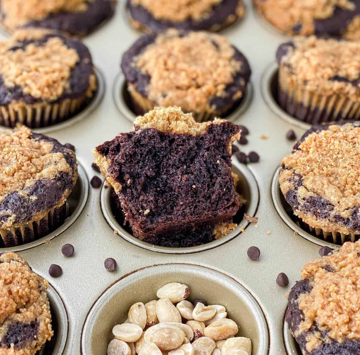 Chocolate Peanut Butter Muffins in a pan with scattered peanuts and chocolate chips.