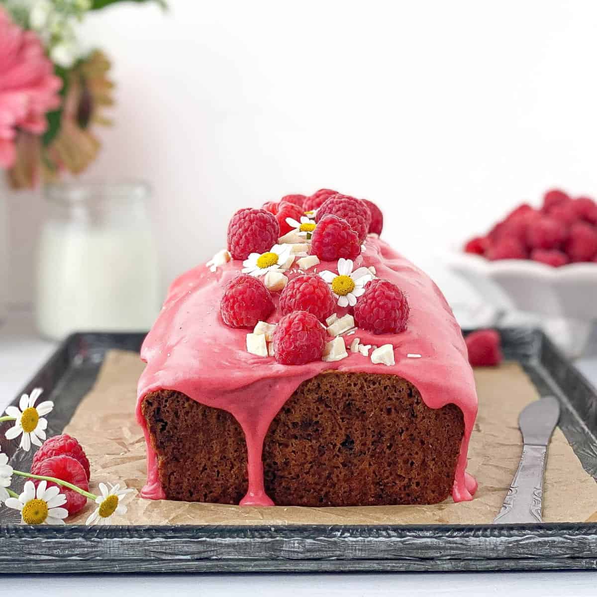 Raspberry and White Chocolate Loaf Cake on a tray with raspberries and white chocolate on top.