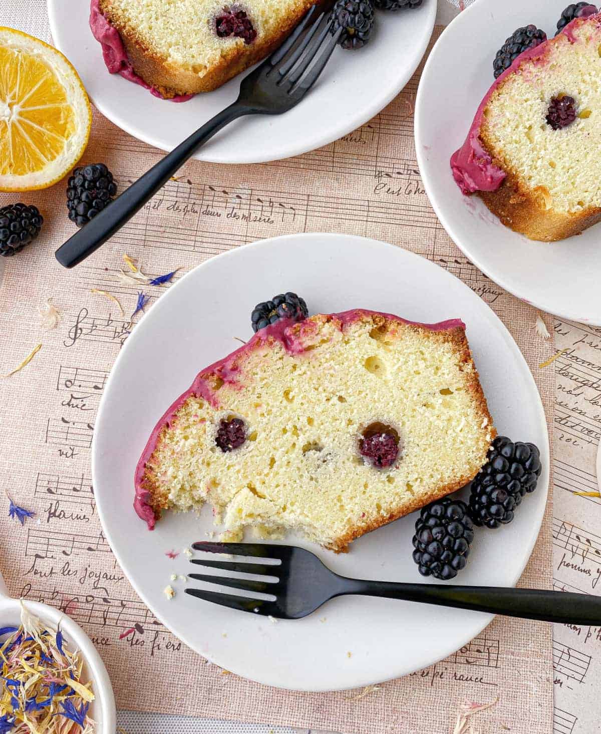 Partially eaten slice of Blackberry Lemon Bread on a white plate with a black fork next to it.