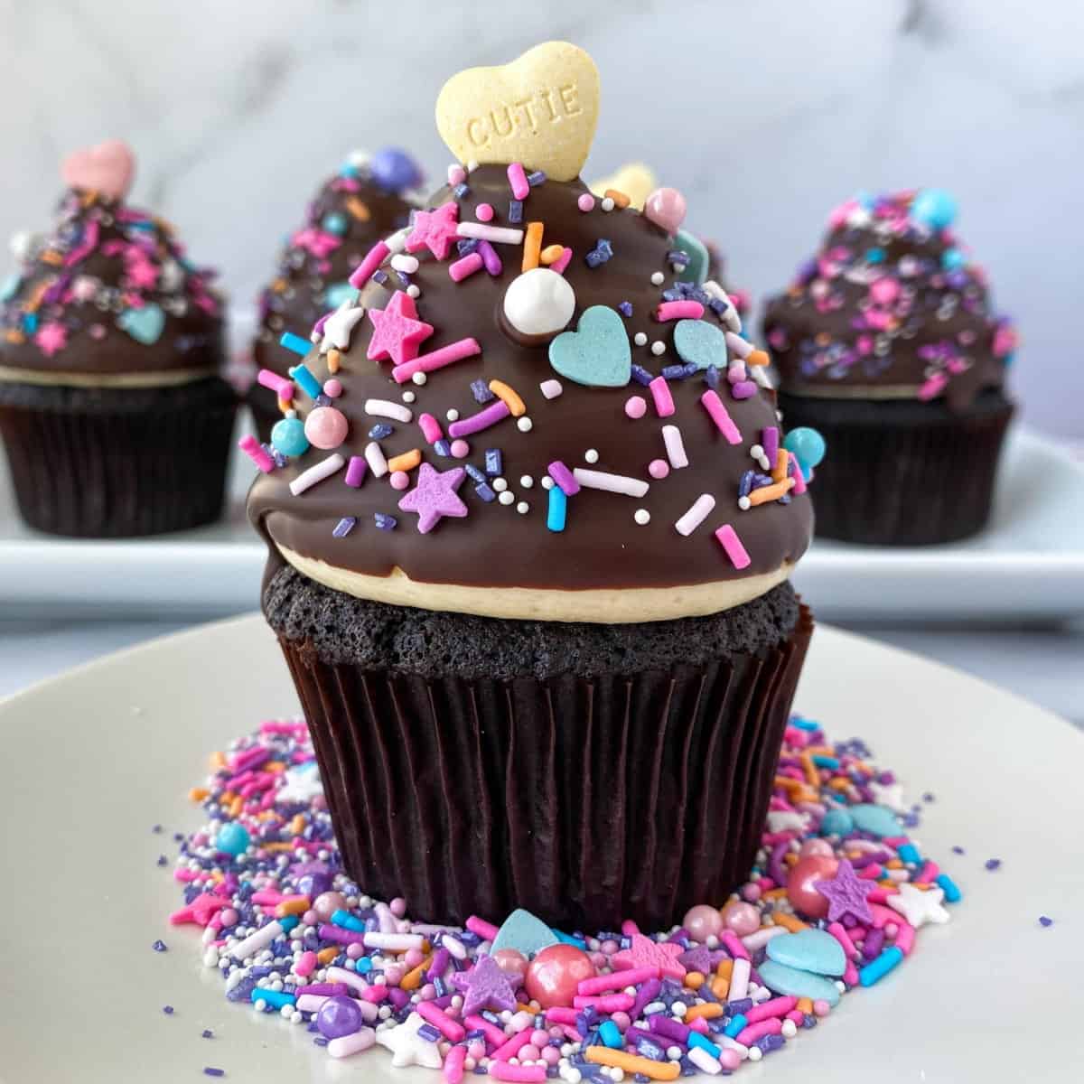 High Hat Cupcake on a white plate with sprinkles on top and around it.