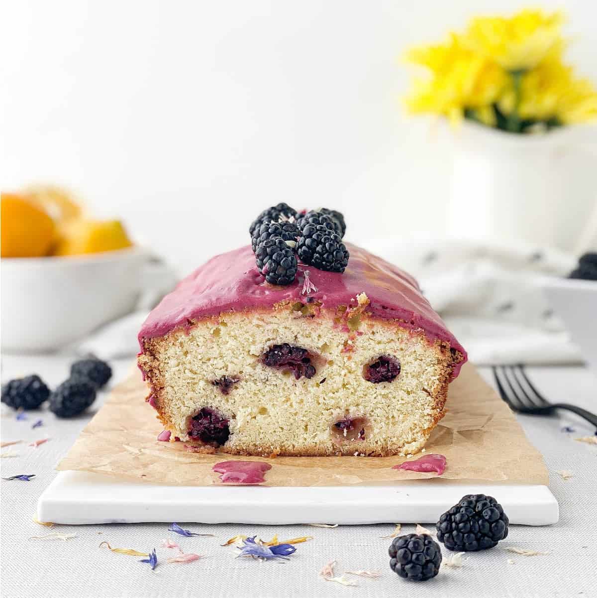 Sliced Blackberry Lemon Bread on a white tray with blackberries and lemons nearby.
