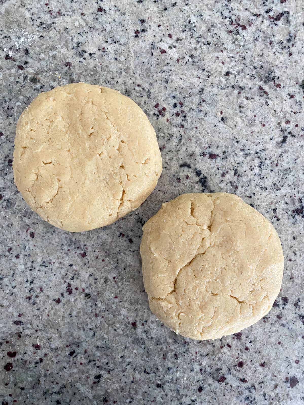Two discs of cream cheese sugar cookie dough on a kitchen counter.