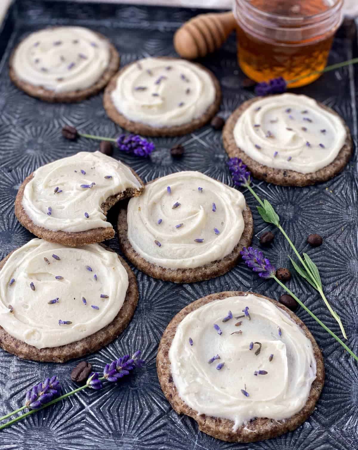 Frosted Honey Lavender Latte Cookies on a pan with fresh lavender, coffee beans, and a jar of honey.
