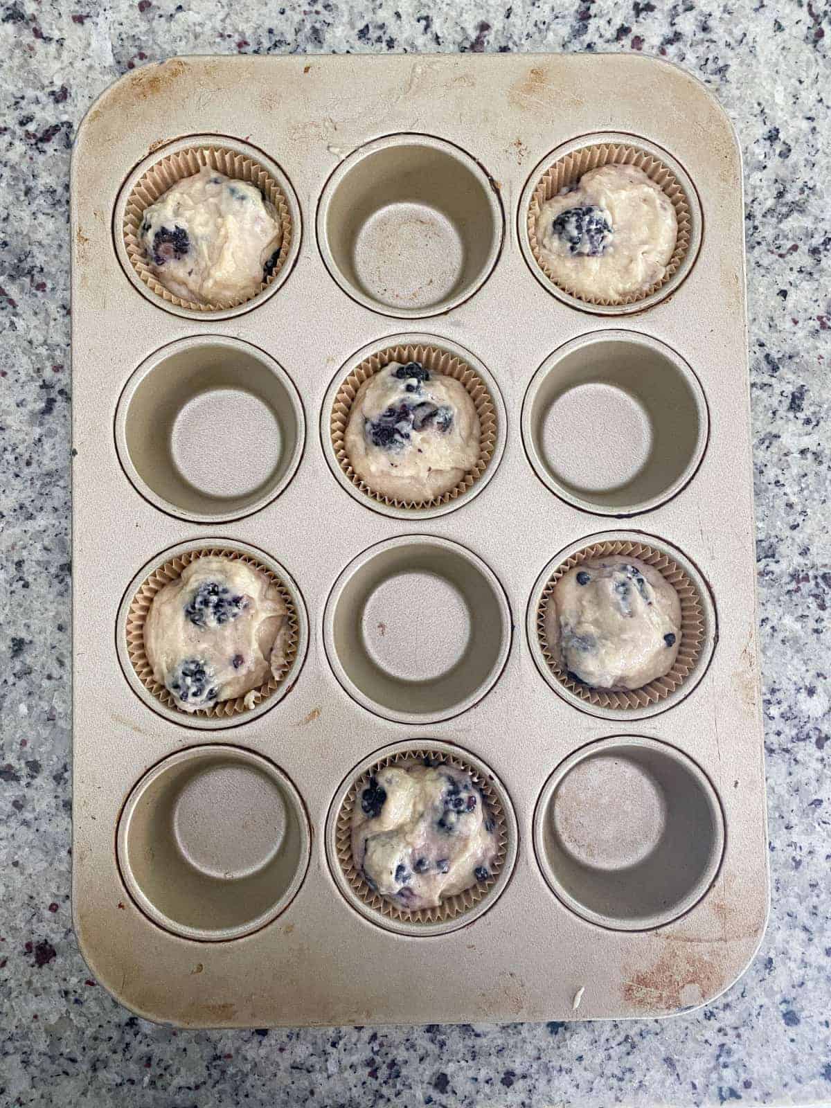 Top view of Blackberry Buttermilk Muffin batter in every other cup of muffin pan.