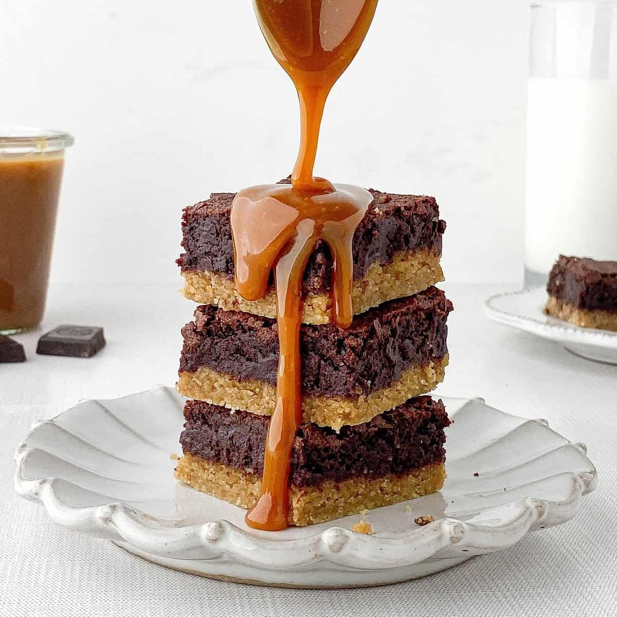 Stack of Blondie Brownies on a white plate being drizzled with salted caramel sauce.