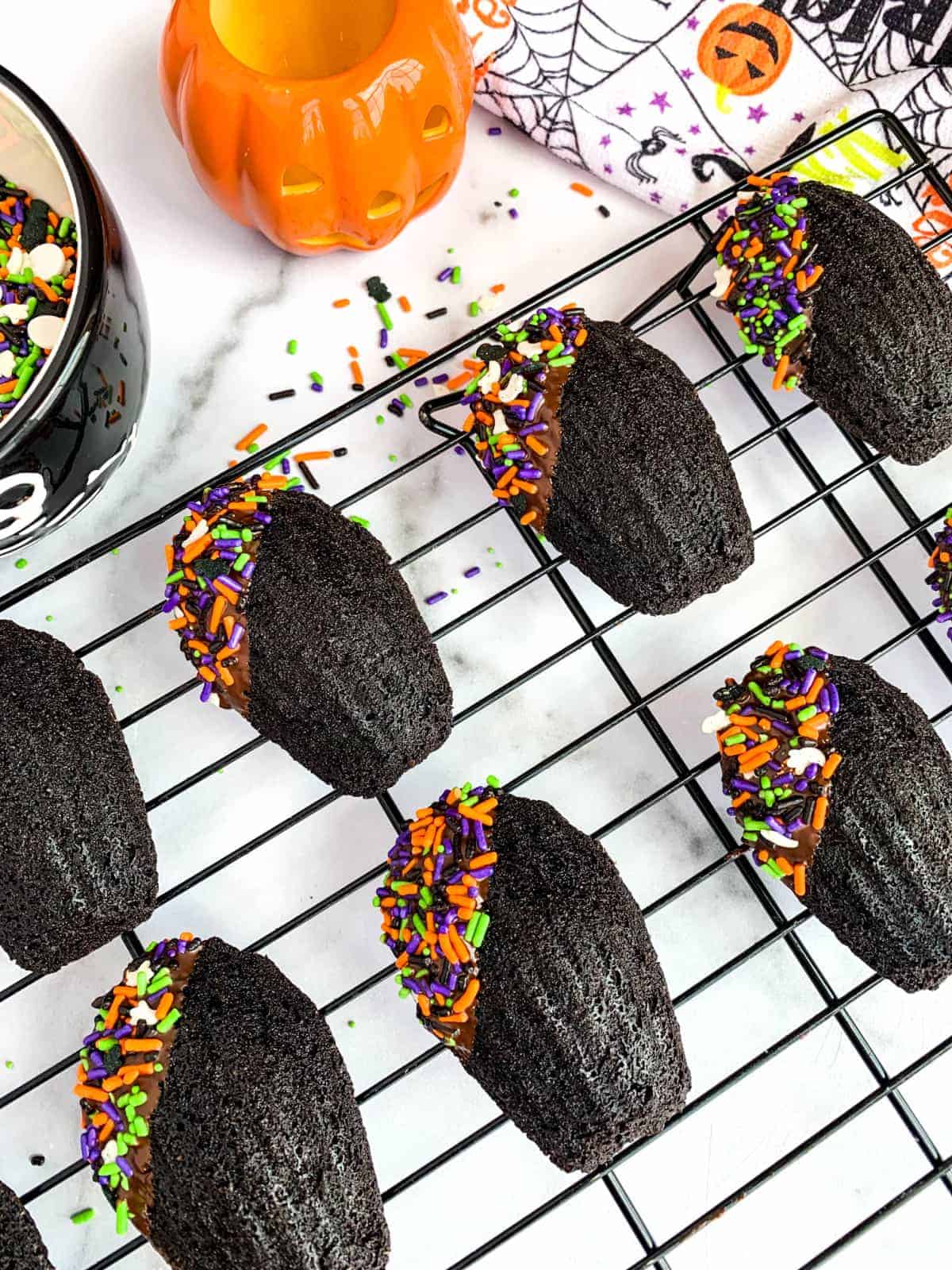 Chocolate Madeleines with Halloween sprinkles on a black cooling rack.