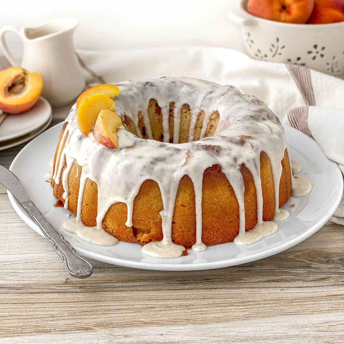 Peach Cobbler Pound Cake on a white serving plate with fresh peach slices on top.