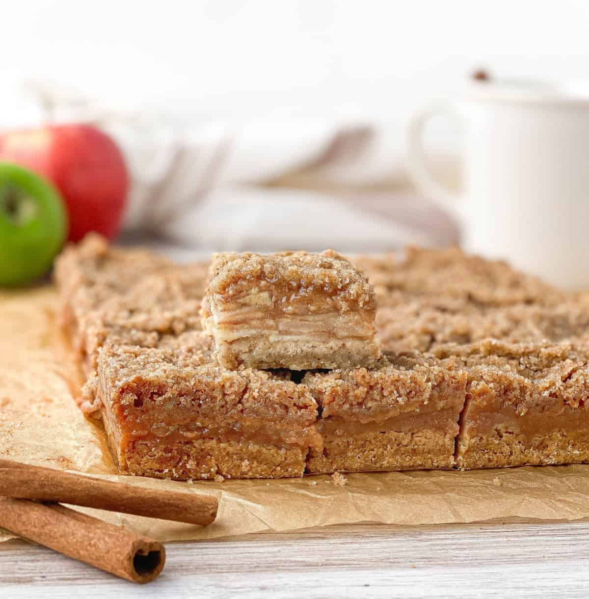 Side view of sliced Apple Crisp Macchiato Bars with apples in the background.