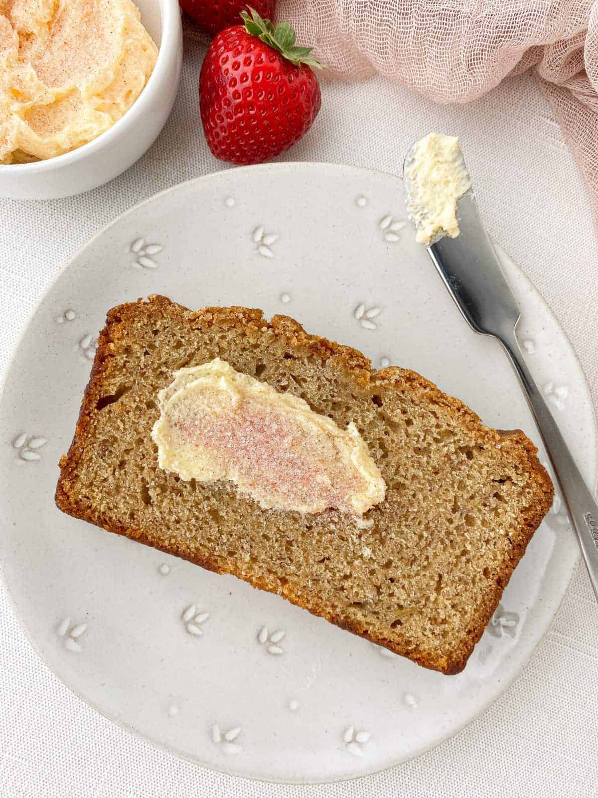 Slice of banana bread with strawberry sugar butter on a white plate.