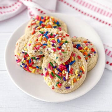 Sprinkle Cookies stacked on a white plate with a bite missing.