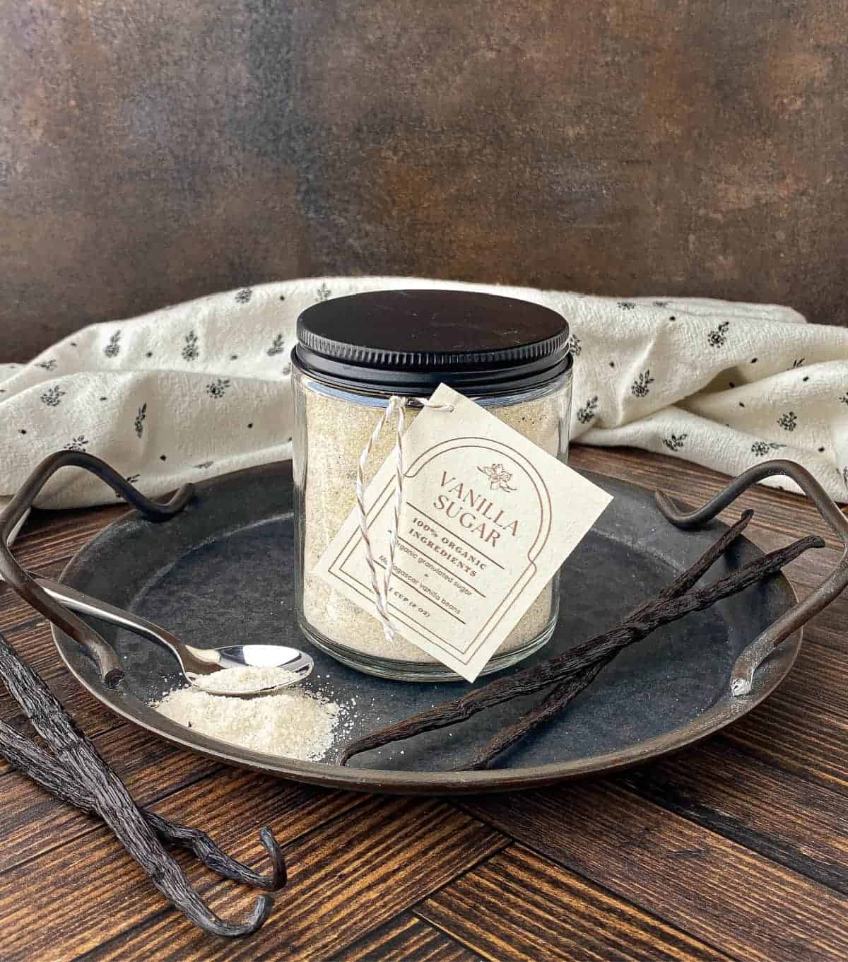 Jar of Vanilla Sugar on a metal tray with vanilla beans.