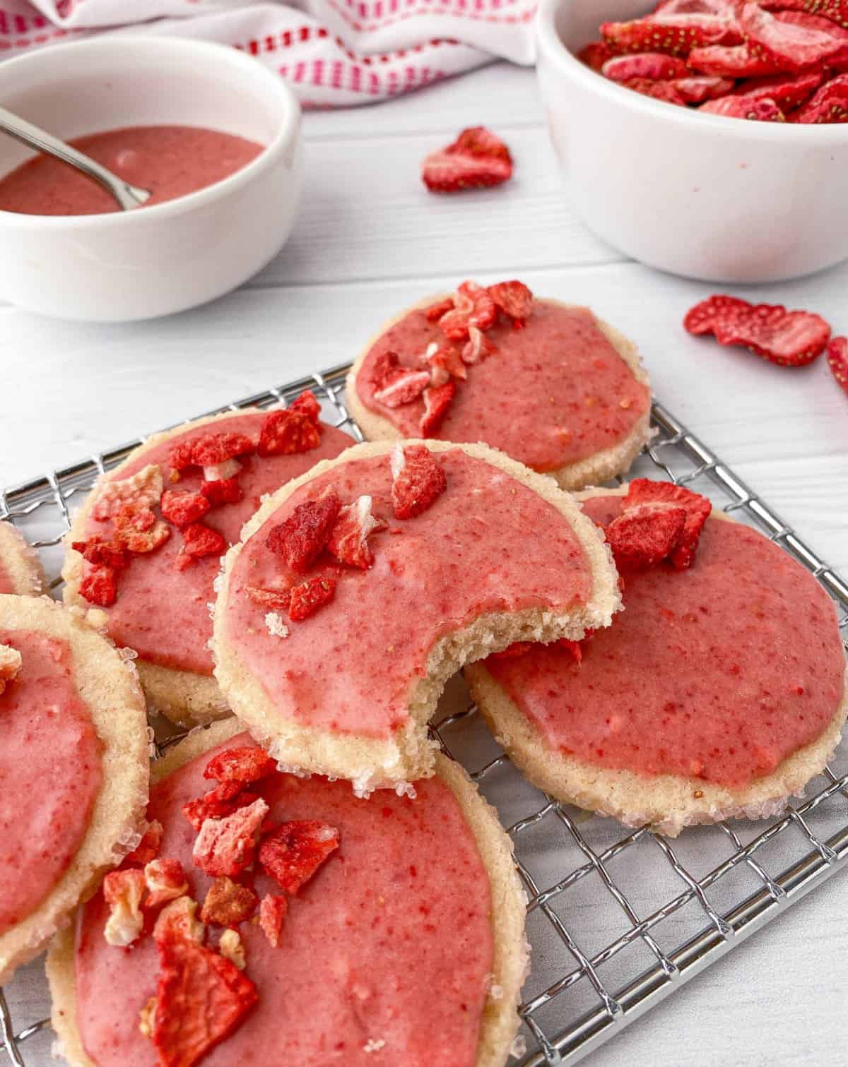 Strawberry Shortbread cookies stacked on a cooling rack, one with a bite missing.