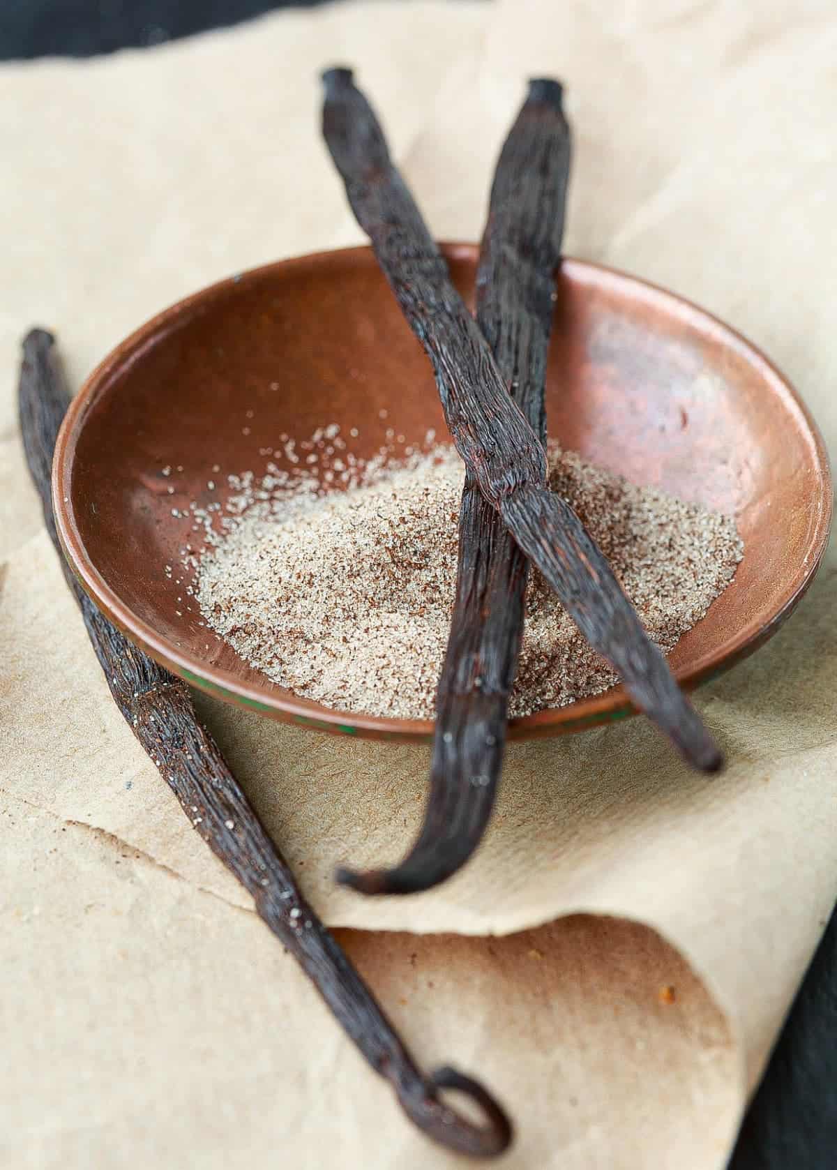 Copper bowl of Vanilla Sugar with vanilla beans on top.