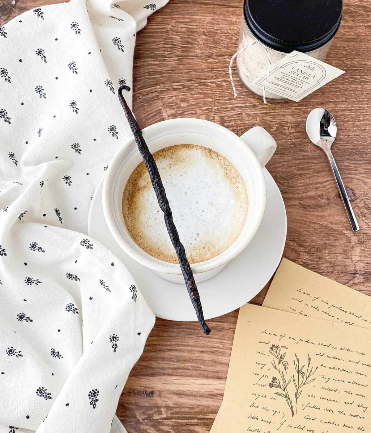 Top view of vanilla latte in a white mug with a vanilla bean on top.