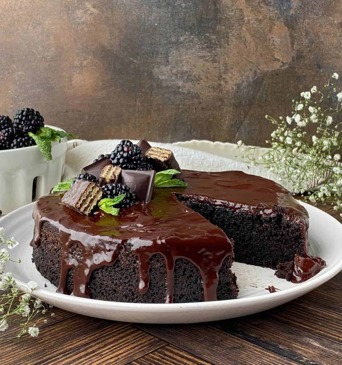 Sliced Chocolate Ganache Cake with chocolate, blackberries, and fresh mint on top.