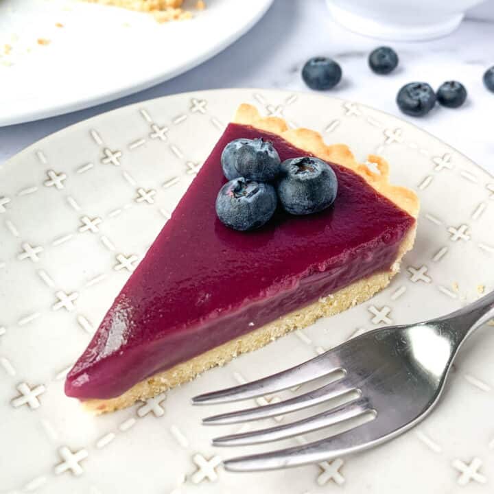 Slice of Blueberry Curd Tart on a white plate.