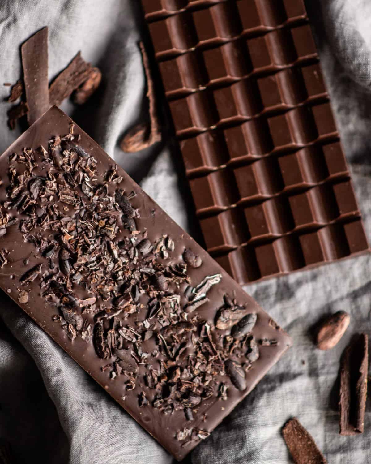 Dark chocolate bars with cocoa beans and shards of chocolate sprinkled nearby.