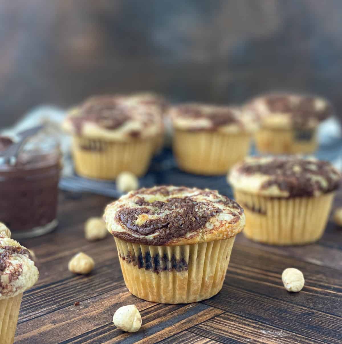 Nutella Muffins with hazelnuts scattered nearby on a wood table.