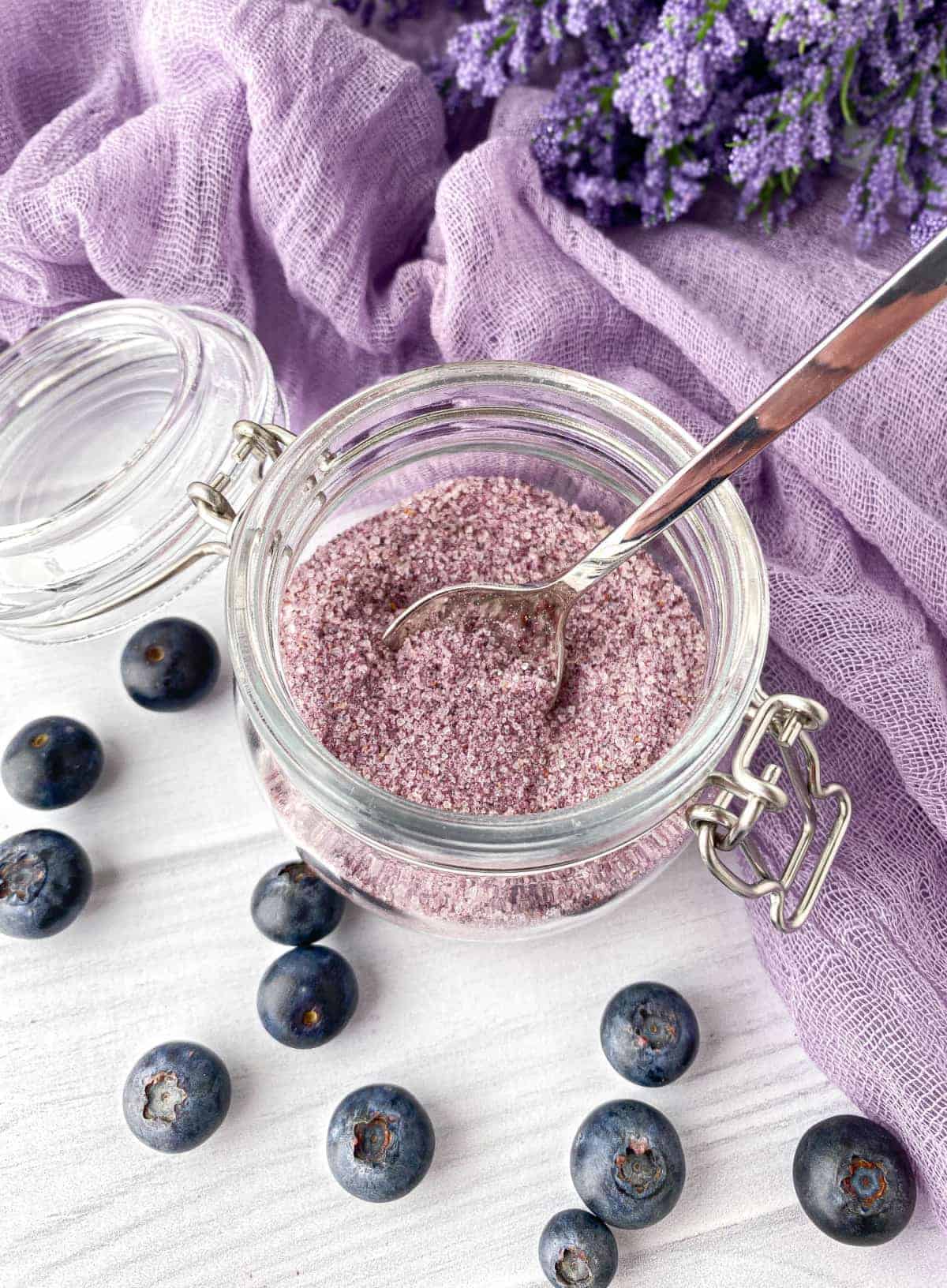 Jar of Blueberry Sugar with fresh blueberries scattered nearby.