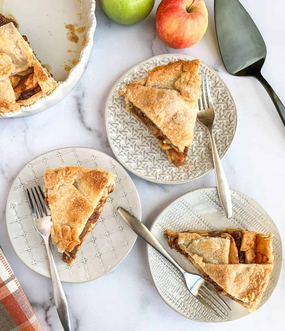 Top view of three slices of Apple Date Pie on textured plates, each with a silver fork.