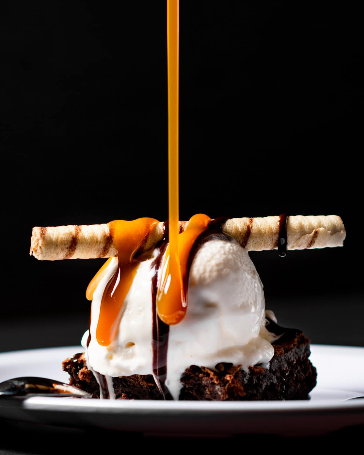 Caramel sauce being drizzled on a brownie sundae.