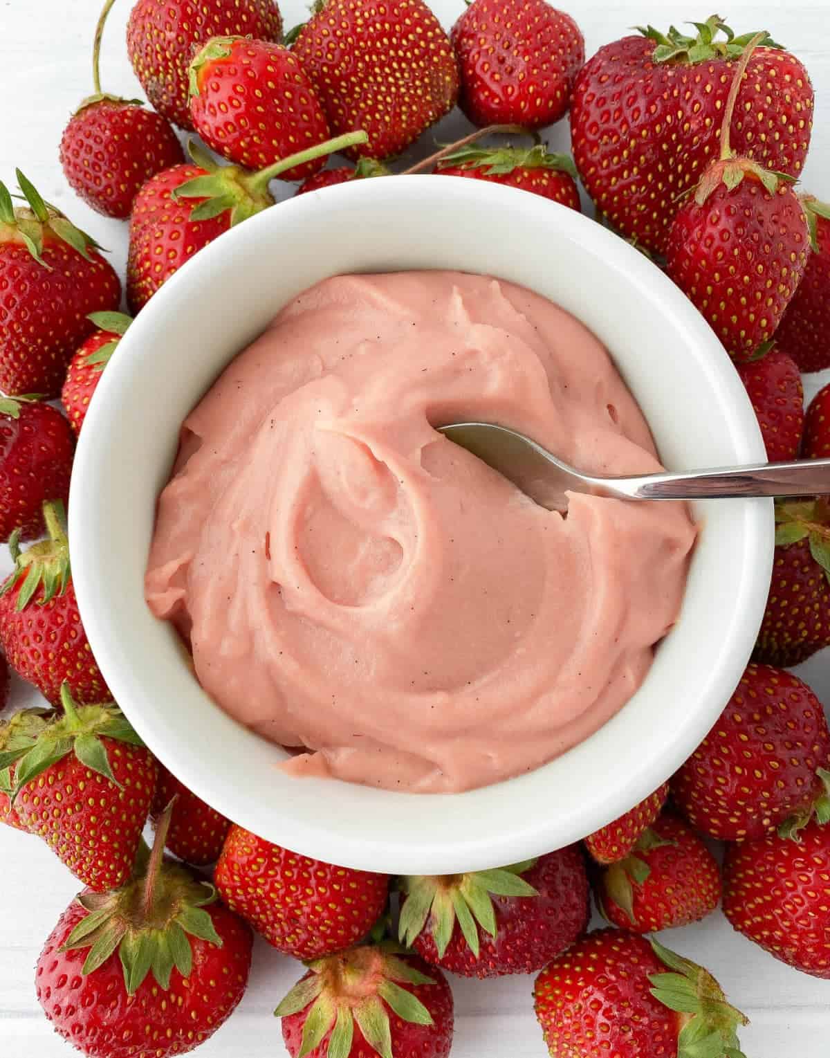 Top view of a white bowl filled with Strawberry Pastry Cream surrounded by fresh strawberries.