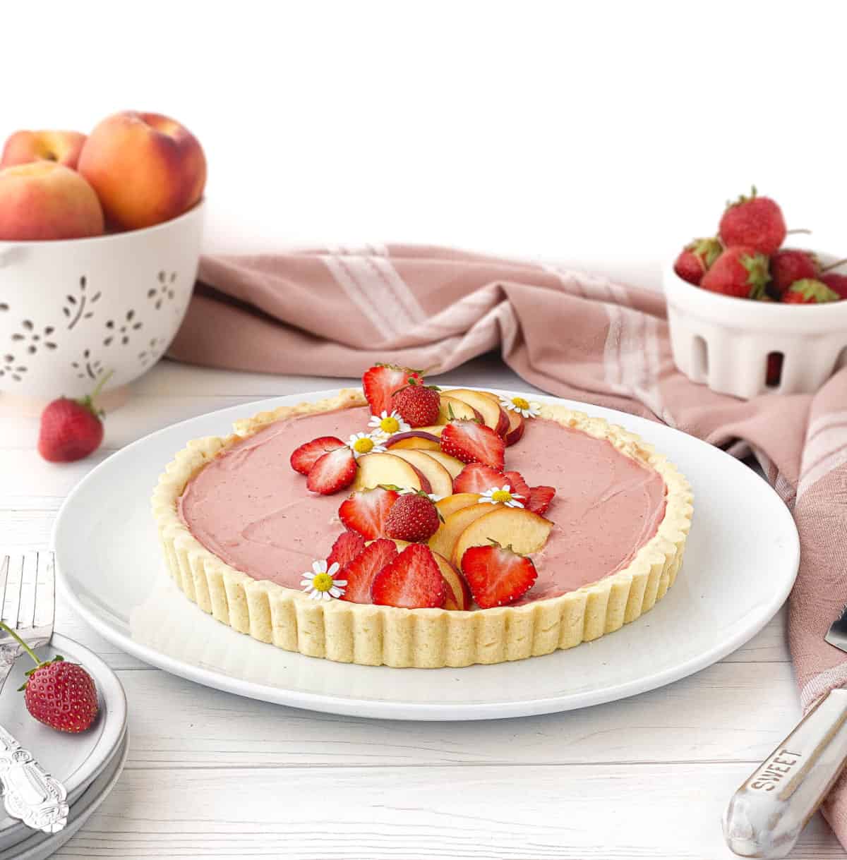 Strawberry Peach Tart on a white serving plate with fresh strawberries and peaches in the background.