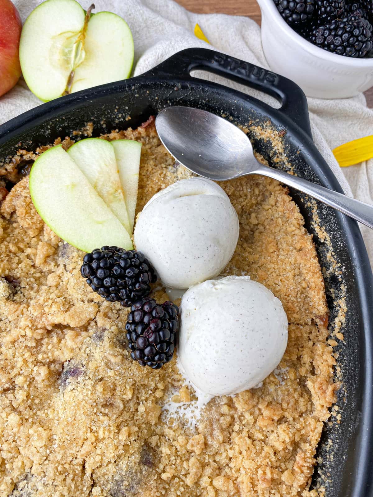 Closeup of Blackberry and Apple Crumble topped with fresh fruit and two scoops of vanilla ice cream.