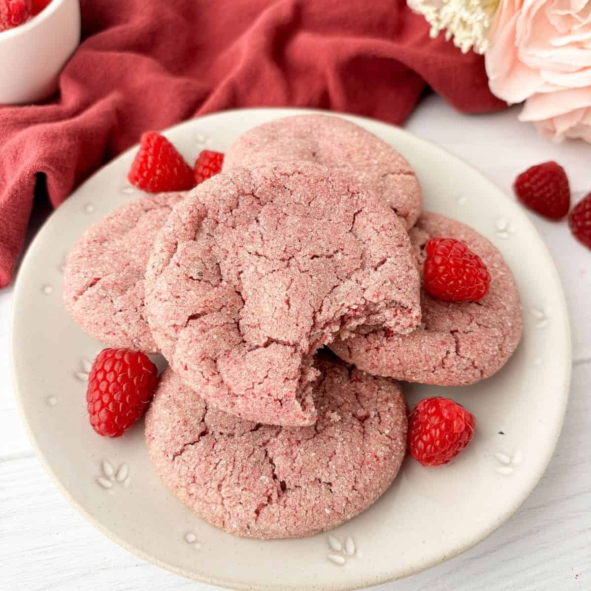 Raspberry Cookies piled on a white plate with fresh raspberries, a bite missing from the top cookie.