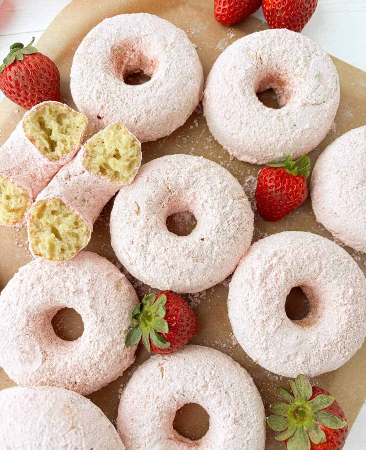 strawberry powdered sugar doughnuts Top view of Strawberry Powdered Sugar Donuts on parchment paper with fresh strawberries.