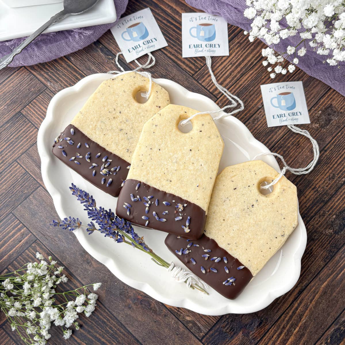 Earl Grey Cookies shaped like tea bags stacked on a white fluted platter.