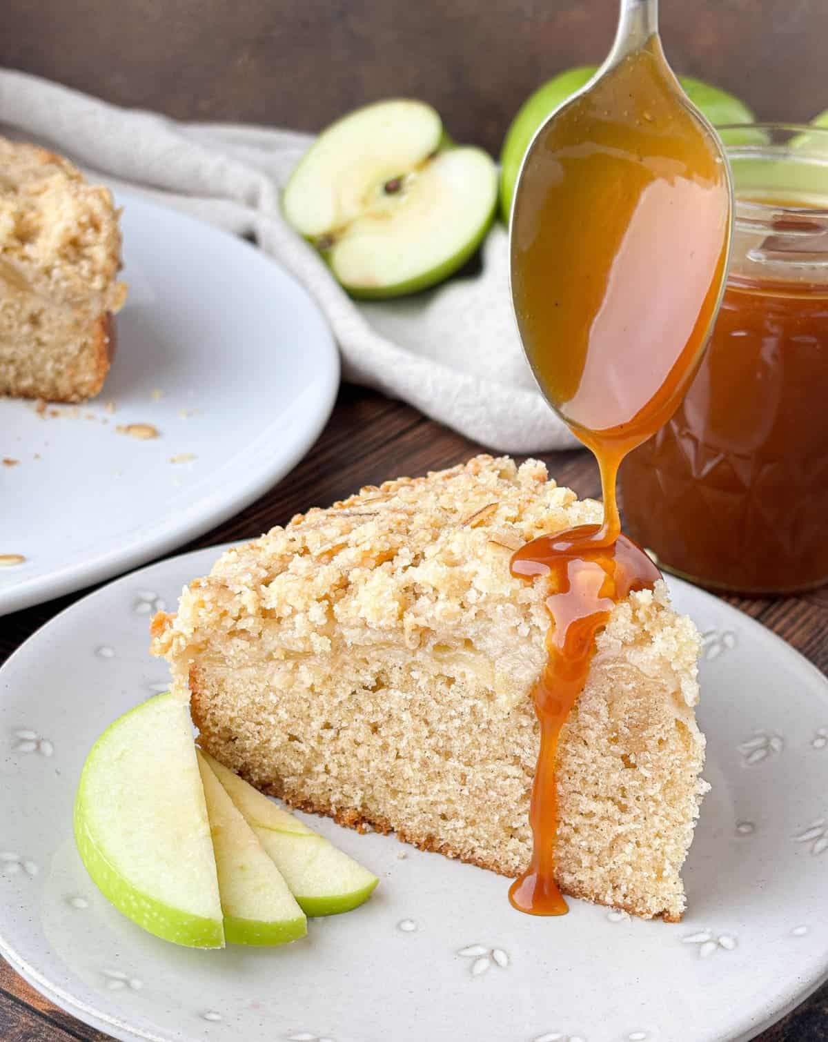 Caramel being drizzled from a spoon onto a slice of Irish Apple Cake on a white plate.