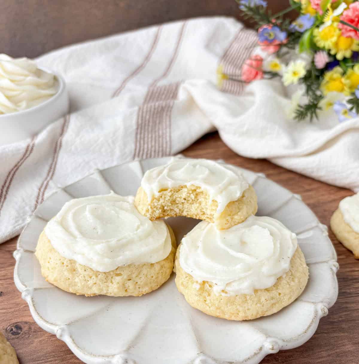 Three Sour Cream Cookies on a white fluted plate, one with a bite missing.