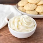 Small white bowl filled with Sour Cream Frosting with cookies in the background.